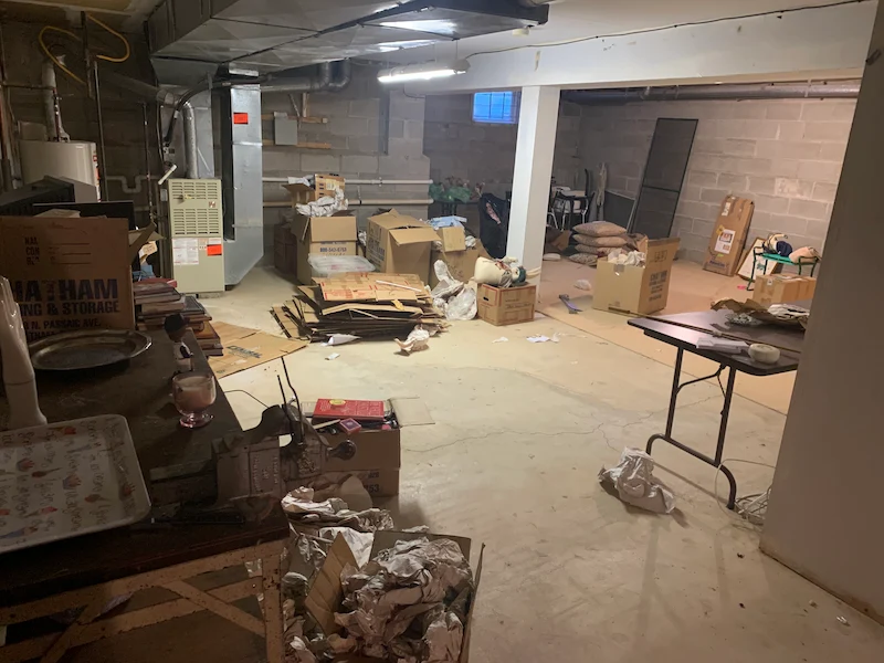 A cluttered basement in Cranford, North Jersey filled with cardboard boxes, packing paper, and miscellaneous household junk before an estate cleanout by JunkDoctors.