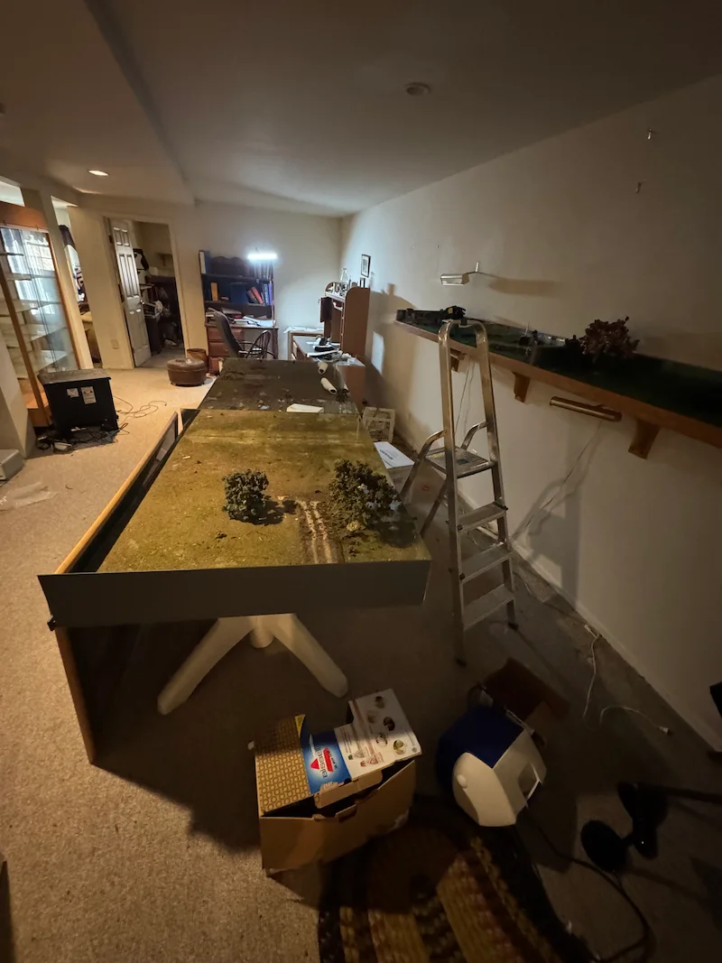 Before photo of a cluttered NJ basement filled with a large custom hobby table and household debris ready for cleanout.