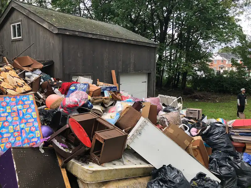 Large scale hoarder property cleanup in Phillipsburg, New Jersey featuring a massive pile of household debris, furniture, and trash bags outside a storage shed.