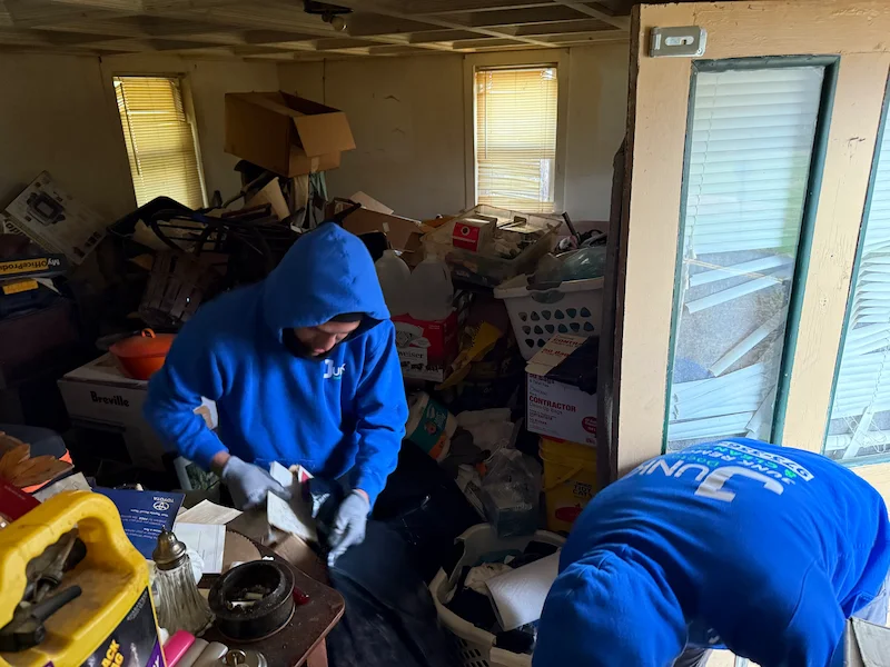 JunkDoctors crew members sorting through heavy floor clutter and old boxes in a low-ceiling residential basement in New Jersey.