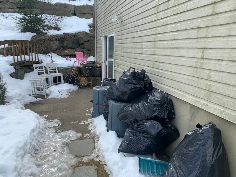 JunkDoctors NJ performing a winter yard cleanup with trash bags, old chairs, and a bicycle being removed from a snowy patio.
